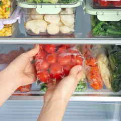 Woman taking plastic bag with frozen tomatoes from refrigerator, closeup