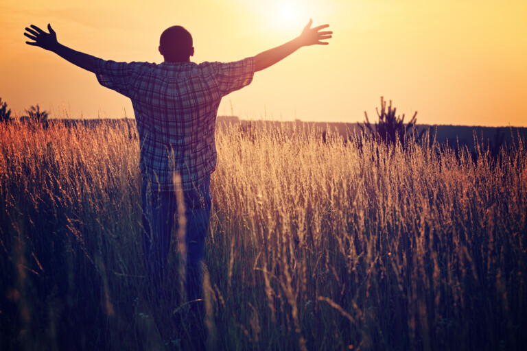Man on the meadow prays to God. The man raises his arms to the sky, his face turned toward the sun. Freedom and religion symbol.