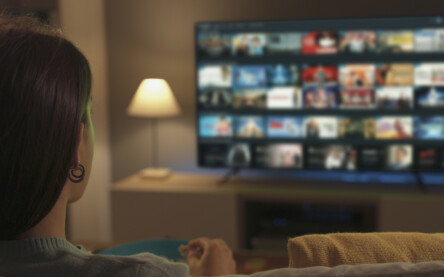 Young woman relaxing on the couch at home and watching videos on demand on her TV, entertainment concept